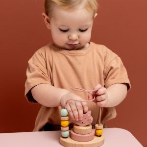 kindje dat aan het spelen is met het roze kat kralenframe van trixie op een roze tafel met rode achtergrond