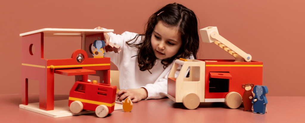 kindje aan het spelen met de houten brandweerwagen en brandweerkazerne van trixie