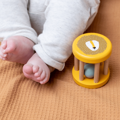 houten rollende rammelaar van trixie op een camel dekentje aan de voetjes van een baby